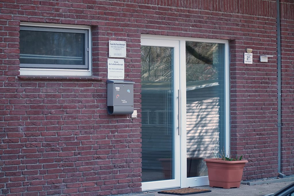 Neben der Praxistür hängen die praxisschilder und der Briefkasten. es ist eine Glastür.
